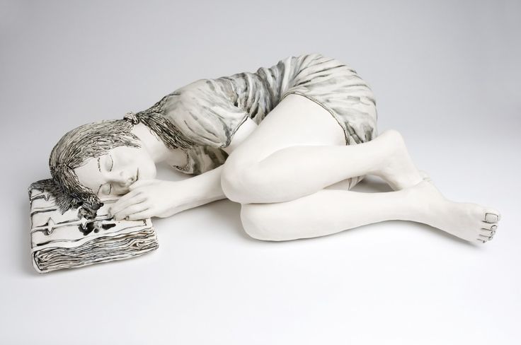 a white statue laying on top of a book next to it's body and hands