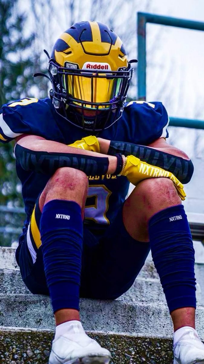 a football player sitting on the steps with his helmet and gloves over his face, holding a baseball bat