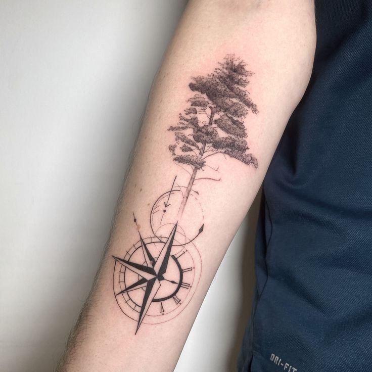 a man's arm with a compass and tree tattoo on the left side of his arm