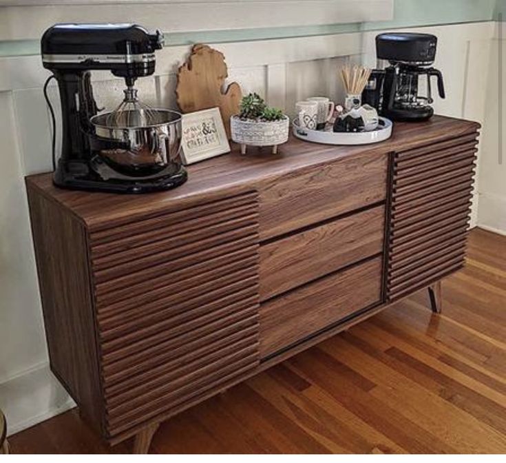 a wooden dresser with coffee maker and other items on it in front of a window