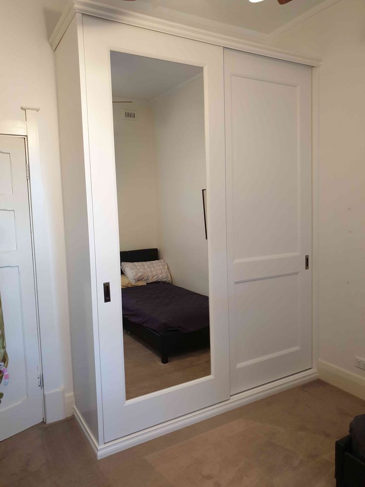 an empty room with a bed and closet doors open to reveal a bedroom in the background