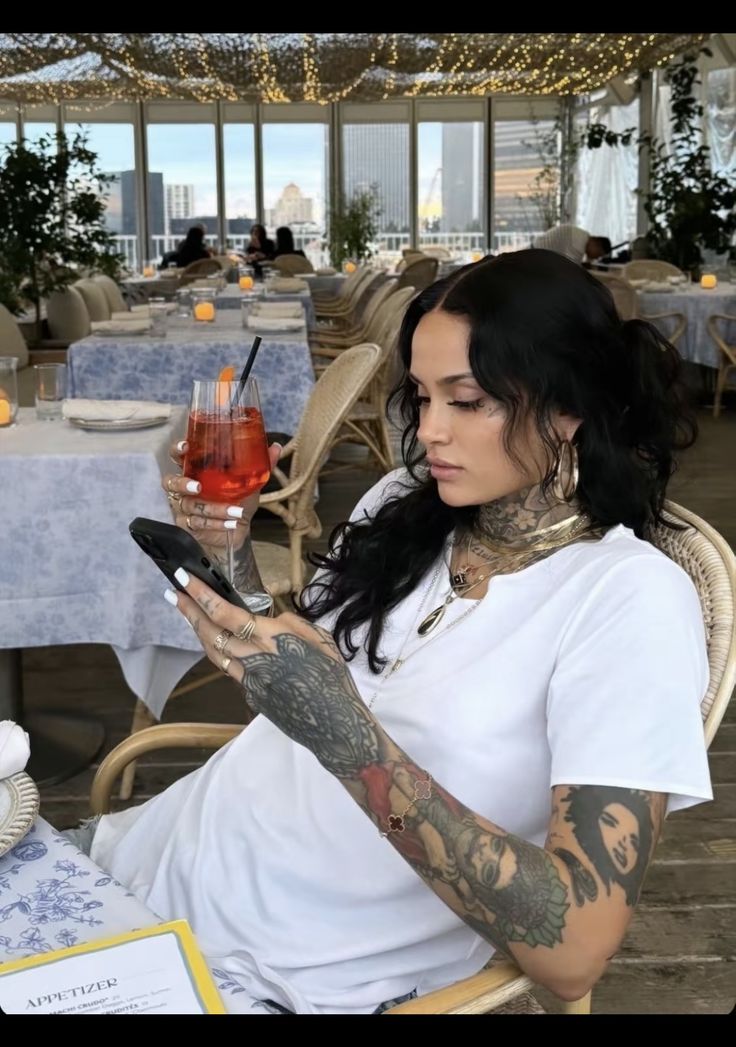 a woman sitting in a chair holding a cell phone and looking at her wrist tattoo