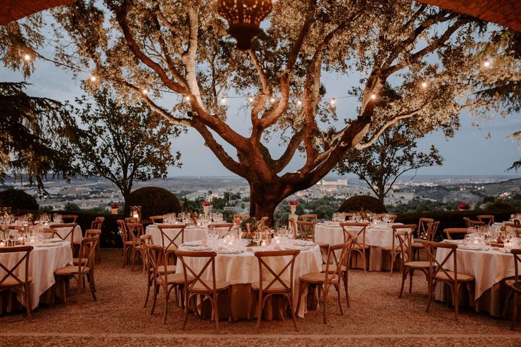 an outdoor dining area with tables, chairs and lights hanging from the trees above it