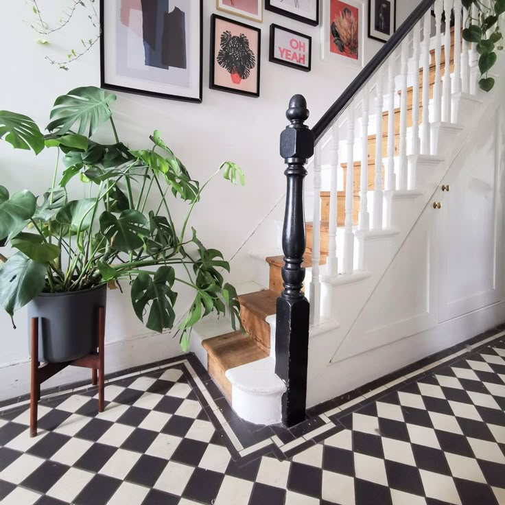 a black and white checkered floor next to a stair case with pictures on the wall