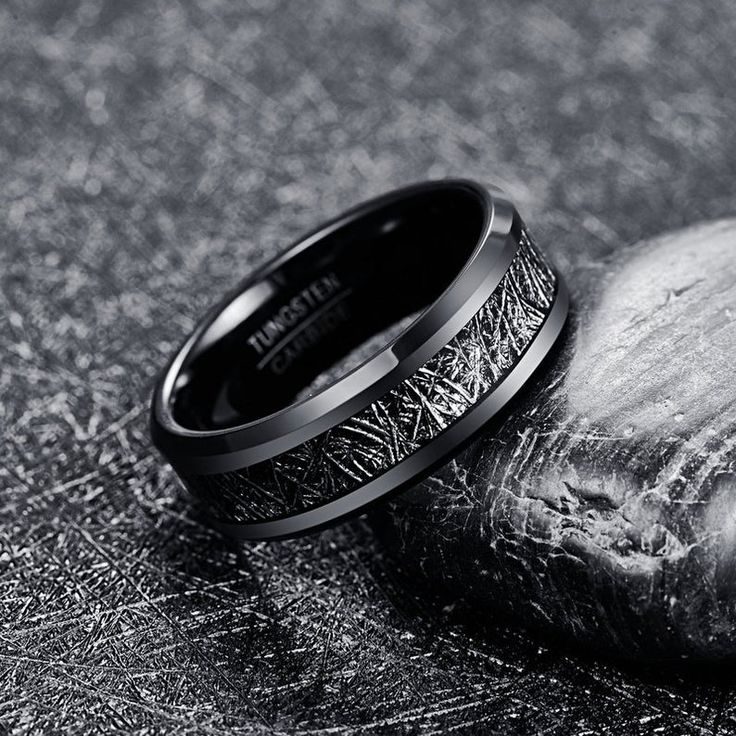 a wedding band with an intricate design on the inside is shown next to a rock