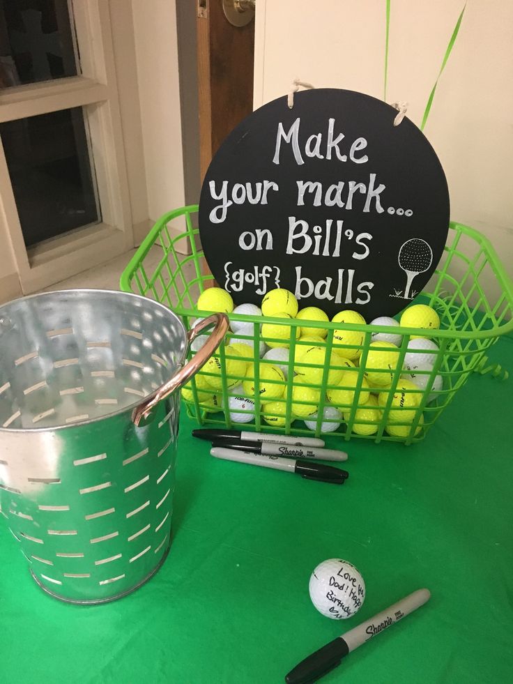 a green table topped with a metal bucket filled with tennis balls and a chalkboard