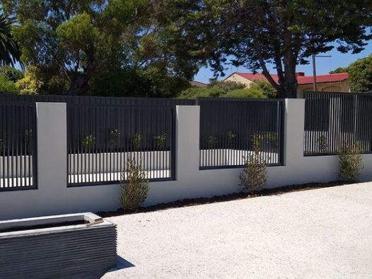 a fenced in area with trees and bushes next to it, along side a building