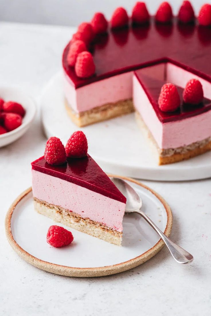 a piece of cheesecake with raspberry topping on a plate next to the rest of the cake