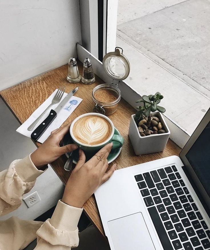 a person sitting at a table with a cup of coffee in front of their laptop