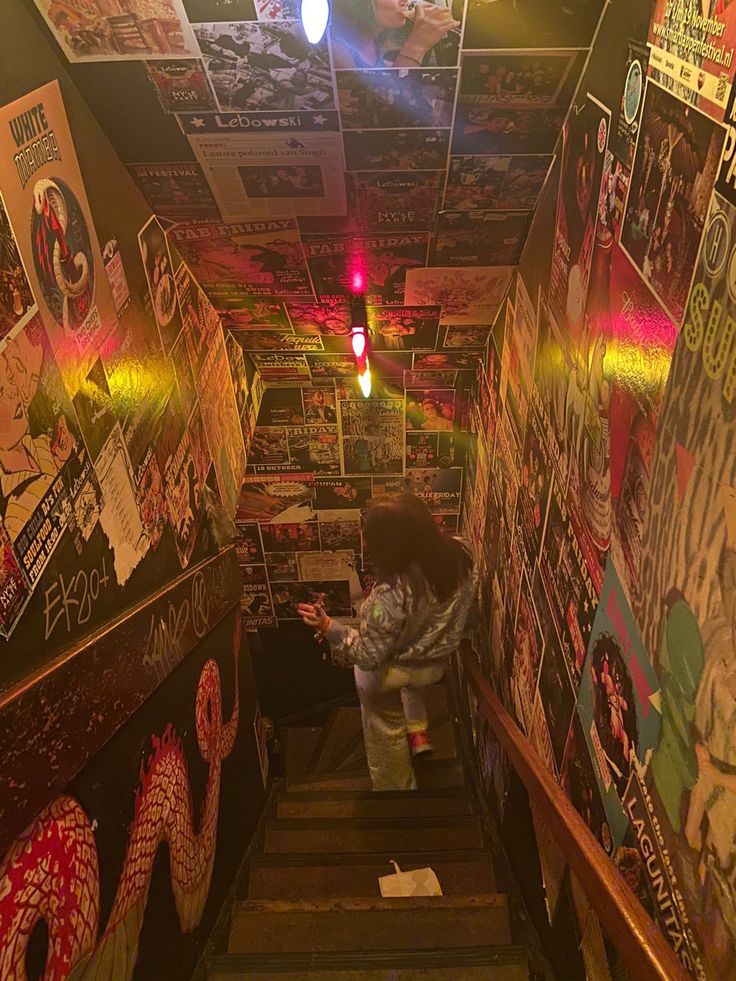 the stairs are covered in graffiti and pictures on the walls, with one person standing at the bottom