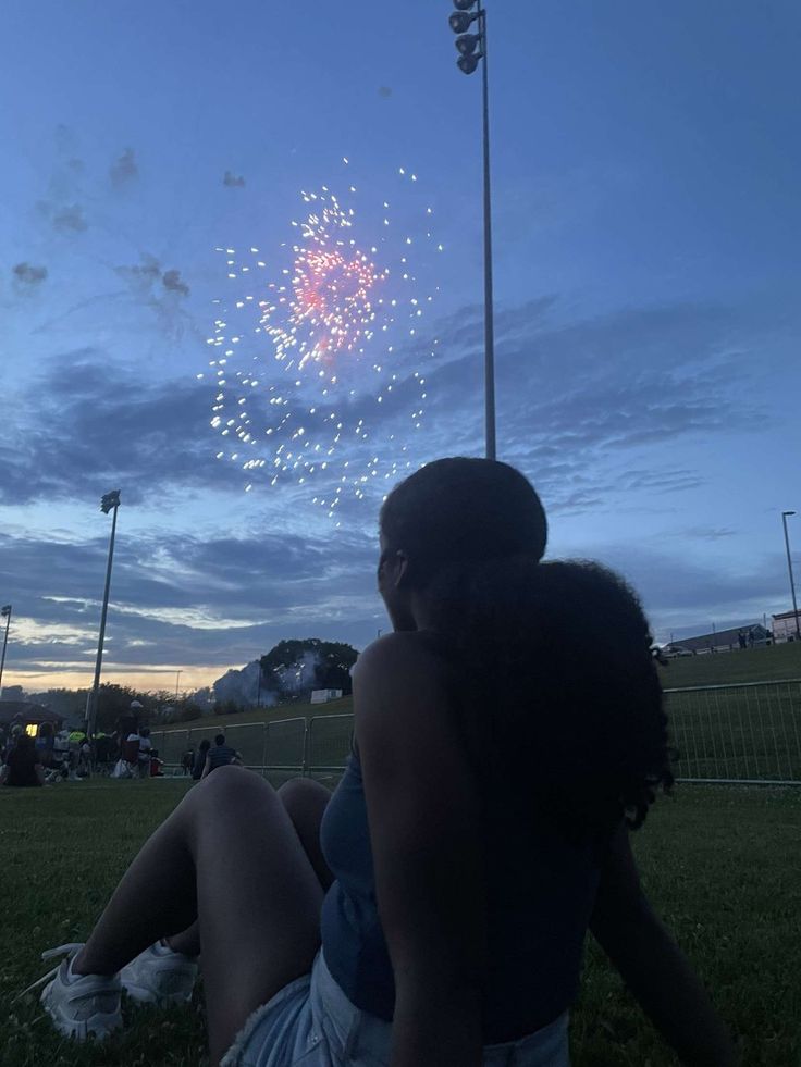 two people sitting in the grass watching fireworks