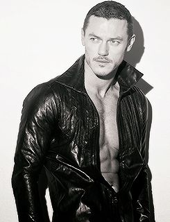 a shirtless man in black leather jacket posing for the camera with his hands on his hips