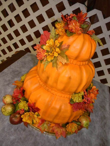 a three tiered pumpkin shaped cake with fall leaves and flowers on the top, sitting on a table