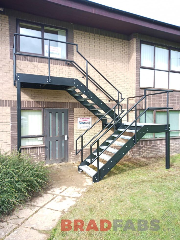 a black metal stair case in front of a brick building with green grass and bushes