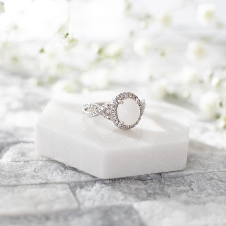 a diamond ring sitting on top of a white marble block with flowers in the background