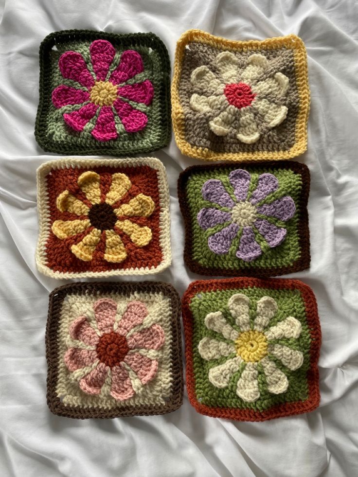 four crocheted squares with flowers on them sitting on a white sheet in the bed