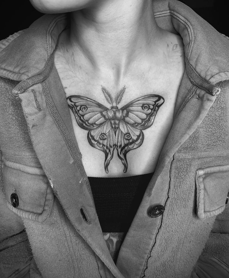 a black and white photo of a woman's chest with a butterfly tattoo on it