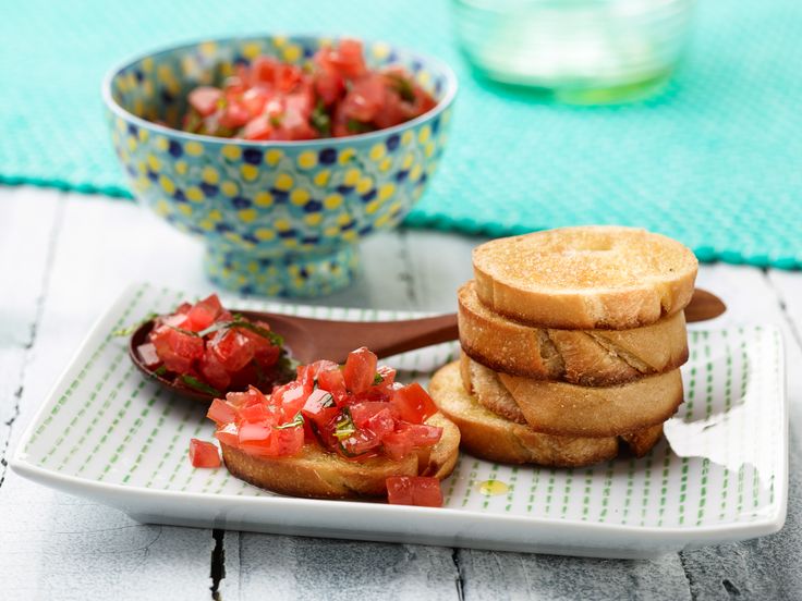 a plate topped with toasted bread and sliced up tomatoes next to a bowl of salad