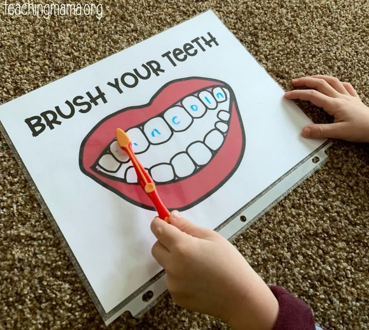 a child holding a toothbrush in front of a sign that says brush your teeth