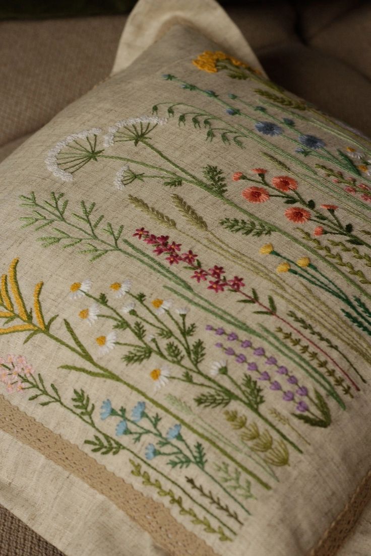 a close up of a pillow on a couch with embroidered flowers and leaves around it