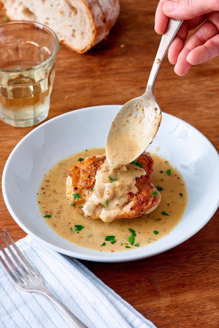 a person is spooning some food out of a white bowl on a wooden table