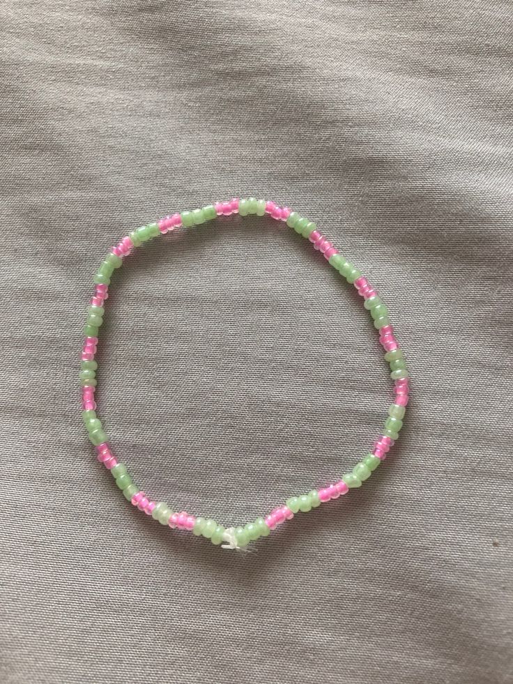 a pink and green beaded bracelet on top of a gray cloth covered bed sheet