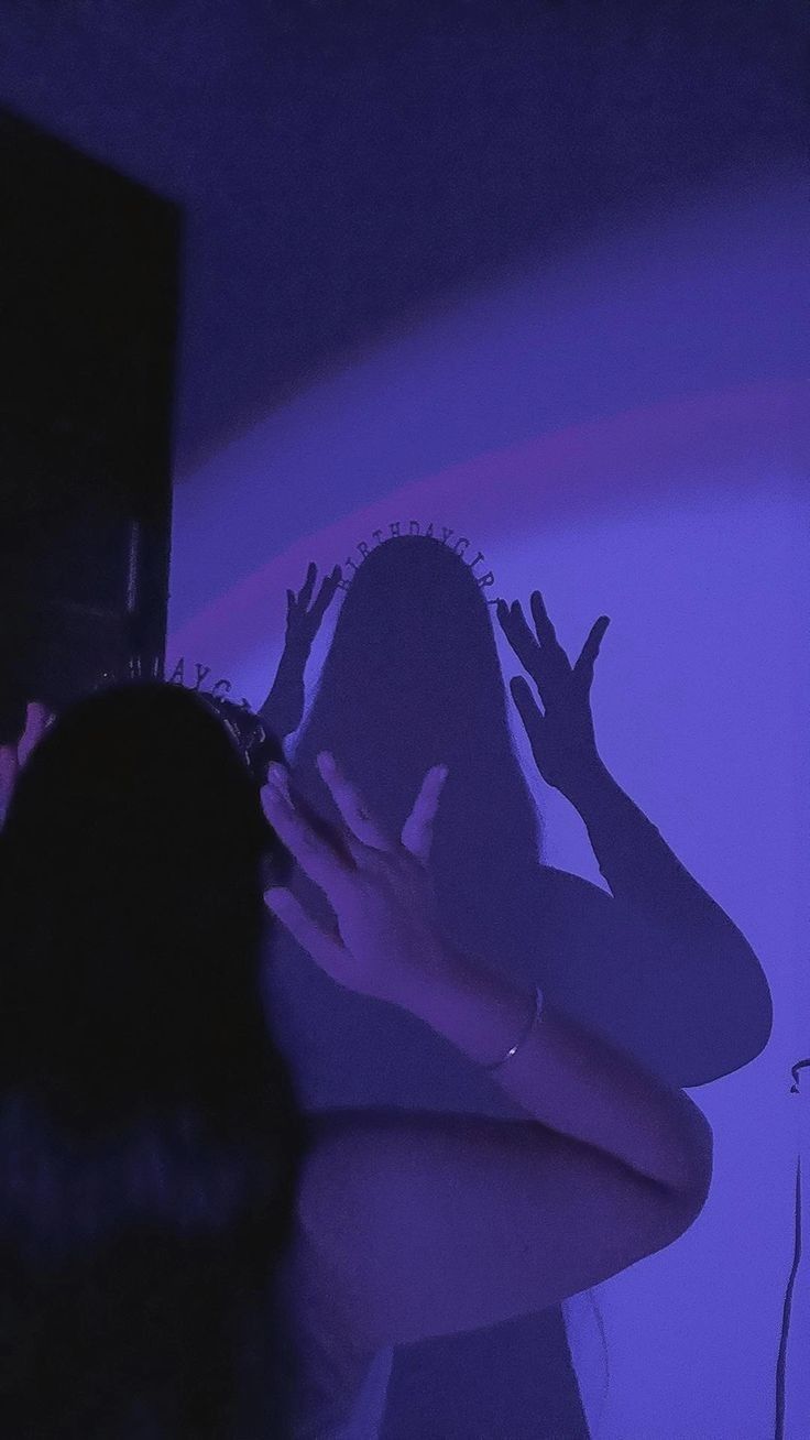 a woman standing in front of a purple light with her hands on her head and arms outstretched