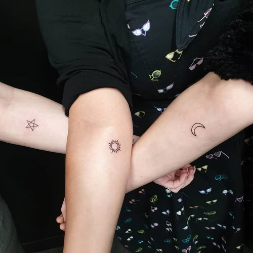 two people with matching tattoos on their arms, one holding the other's arm