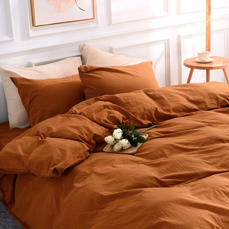 a bed with an orange comforter and pillows in a room next to a window