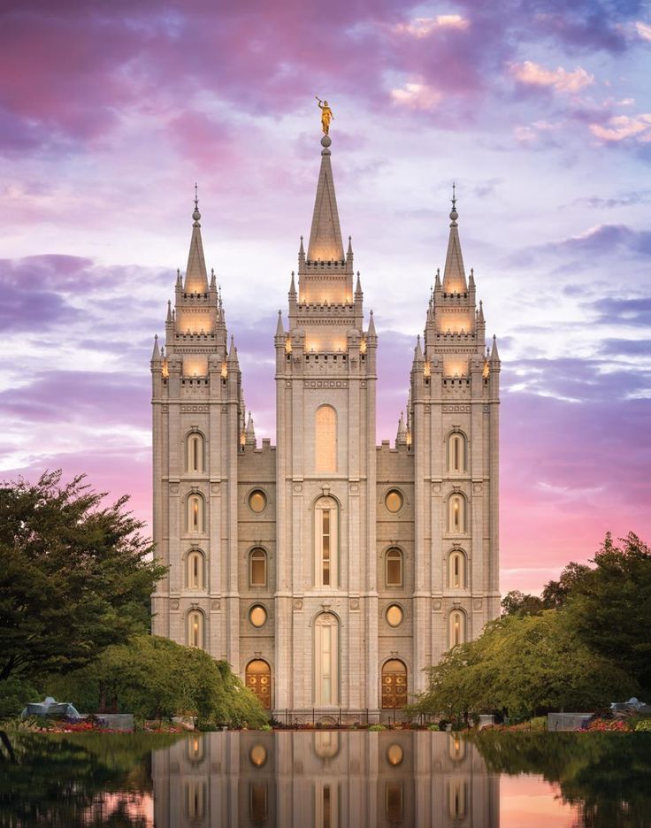 the salt lake temple is lit up at night with its reflection in the still water