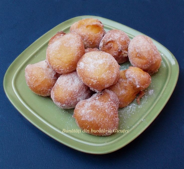 a green plate filled with powdered sugar covered doughnuts on top of a blue table