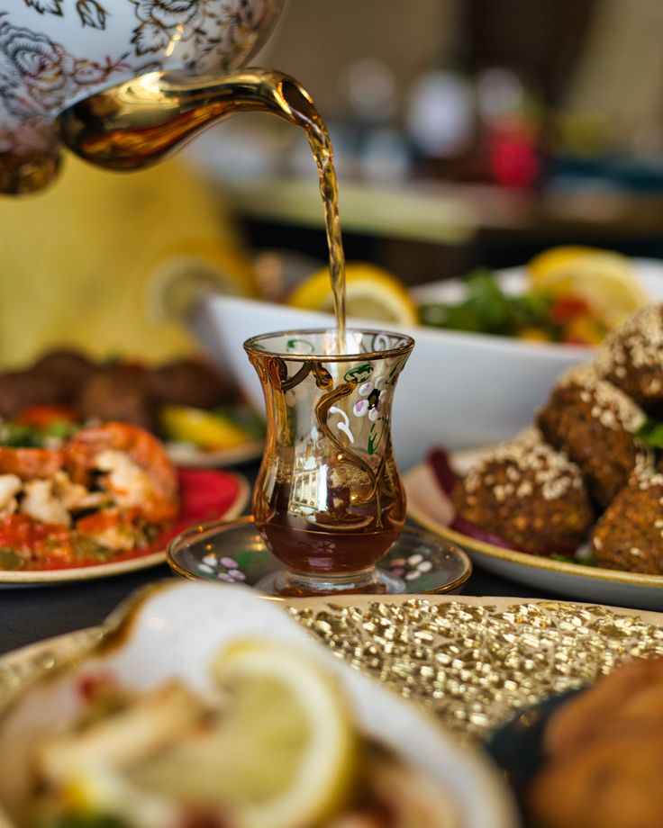 a person pours tea into a glass on a table full of plates with food