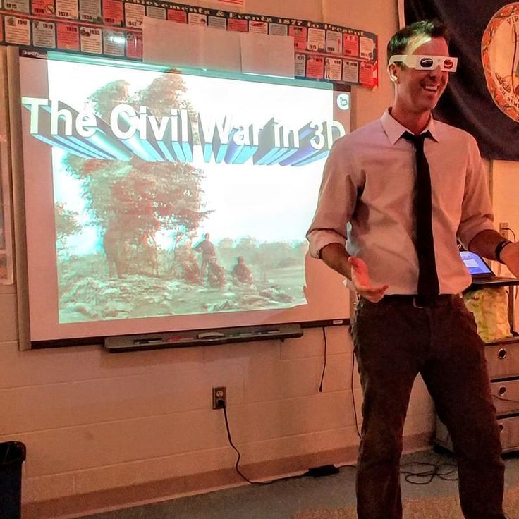 a man standing in front of a projector screen while wearing a tie and glasses