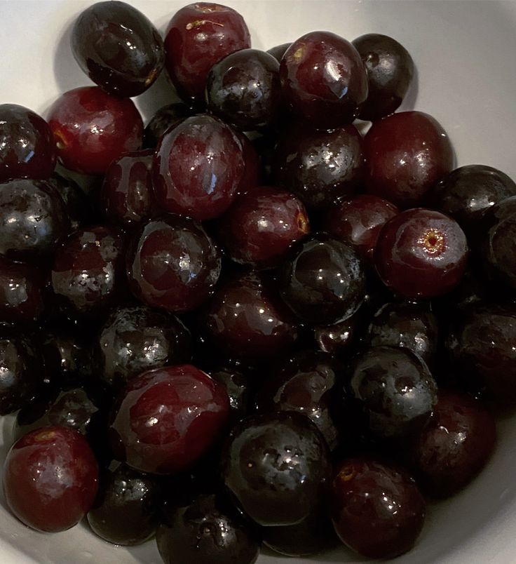 a white bowl filled with plums on top of a table