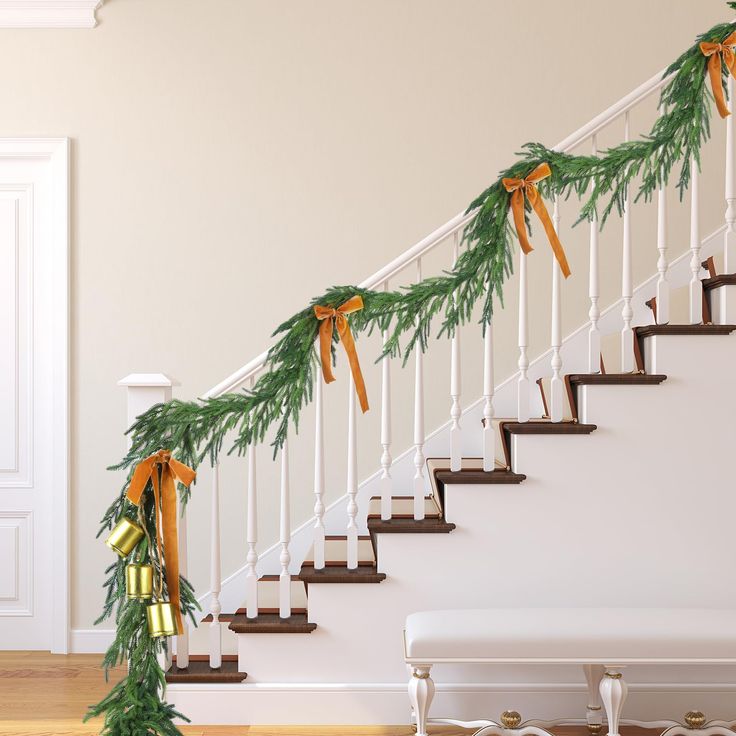 a staircase decorated with pine branches and orange bows for holiday decorations on the banister