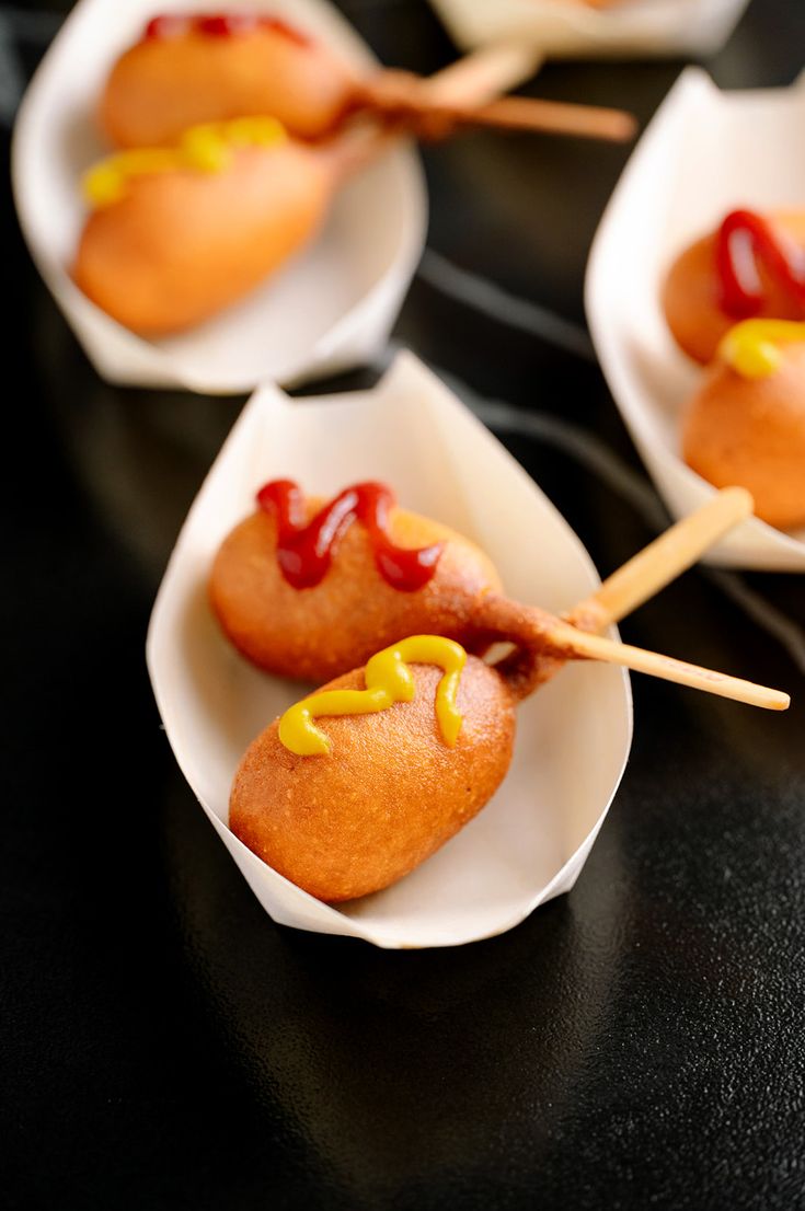 hotdogs with ketchup and mustard on wooden skewers in paper bowls