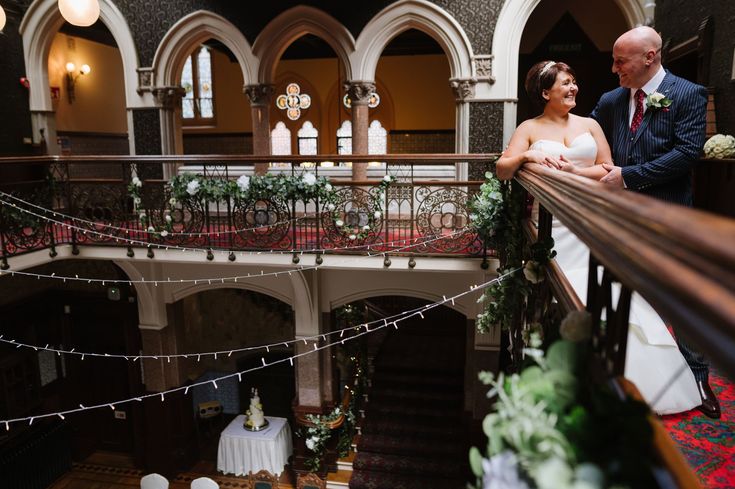 a bride and groom standing on the balcony of their wedding reception venue in an old building