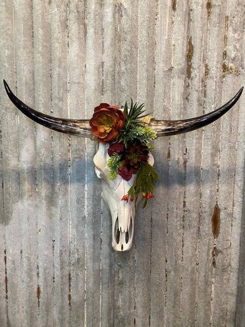 an animal skull with flowers on it's antlers against a metal wall background