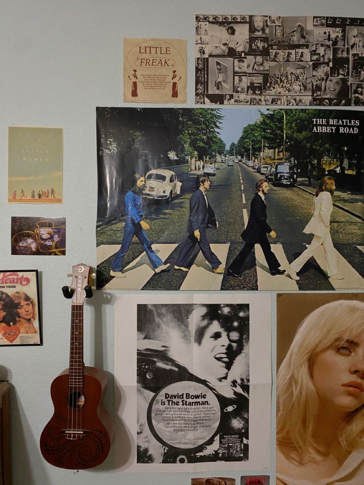 a wall with pictures, posters and a guitar hanging on it's side next to a dresser