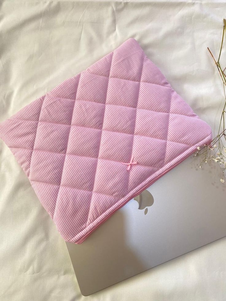 an open laptop computer sitting on top of a white sheet covered in pink quilting