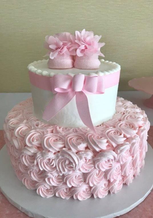 a cake with pink icing and baby booties on top, sitting on a plate