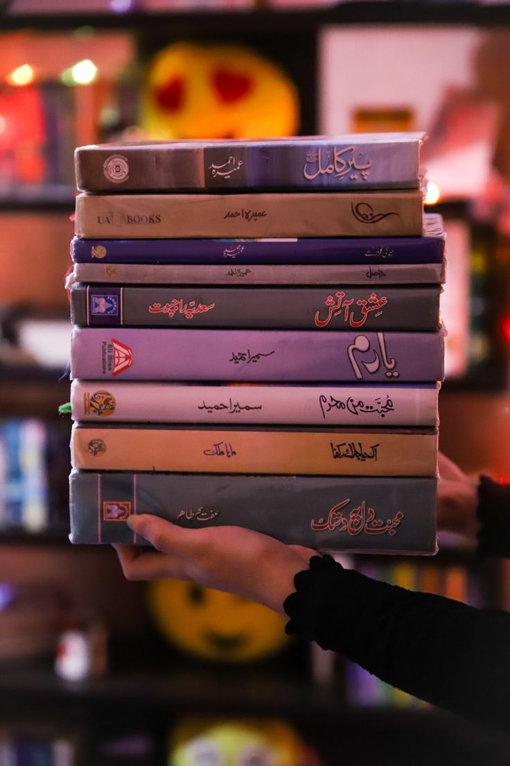 a person holding a stack of books in front of a shelf filled with other books