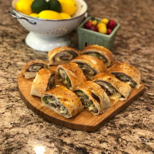 a wooden cutting board topped with pastries next to a bowl of fruit