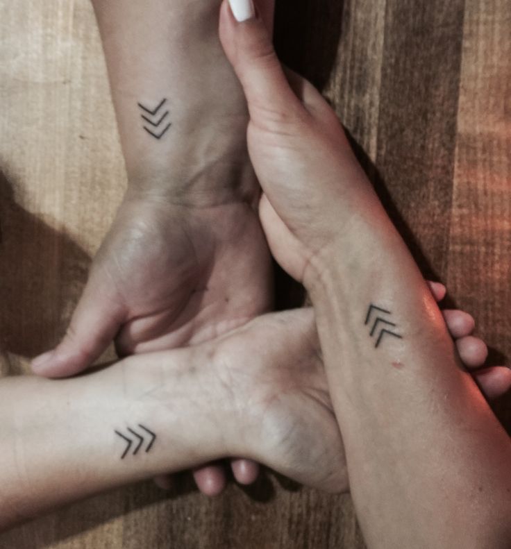 two people holding hands with arrows tattooed on them