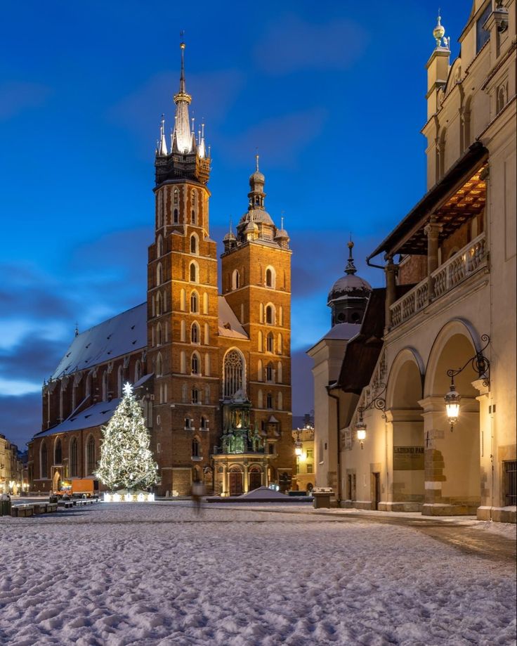 an old building with a christmas tree in the foreground and snow on the ground