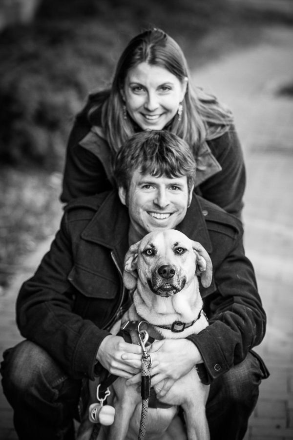 a man and woman are hugging their dog in black and white with a smile on his face