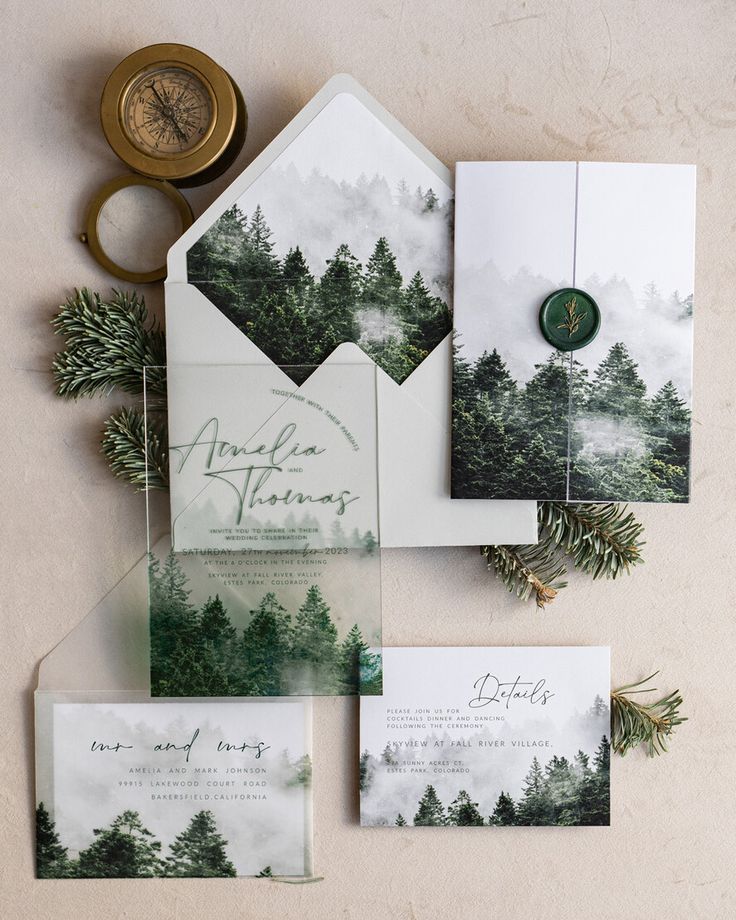 the wedding stationery is laid out on top of each other, with pine trees in the background