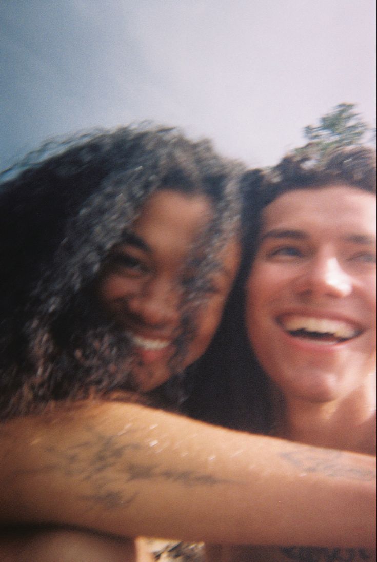 two people smiling and hugging each other with the sky in the back ground behind them