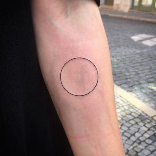 a small black circle tattoo on the arm