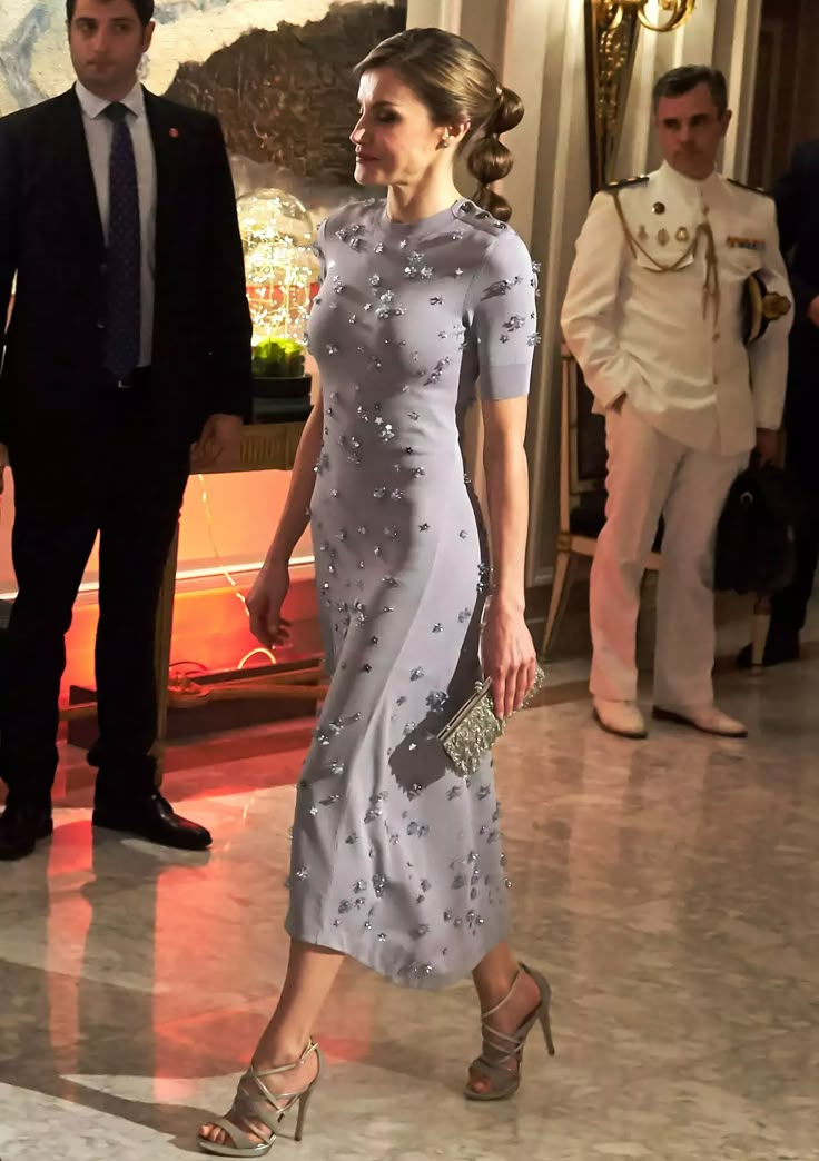 a woman in a gray dress is walking down the hall with other people behind her